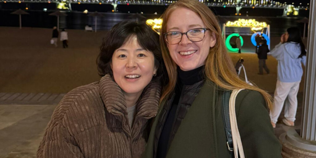 Night-time portrait of two women near a city riverfront, celebrating creative collaboration and storytelling.