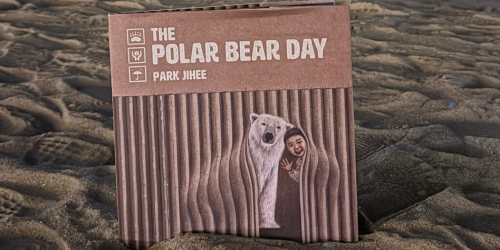 Children’s book titled “The Polar Bear Day” by Park Jihee placed on the beach, showing a child and a polar bear together on the cover.